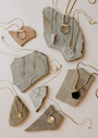JaxKelly's Mystery Necklace features unique gold pendants like crystals, geometric shapes, and eye designs, displayed on stone slabs—an ideal choice for a surprise gift or jewelry deal.
