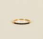 The Half Pave Ring - Black features a slim gold band adorned with a row of small black cubic zirconia stones along the top, showcased on a plain beige background.
