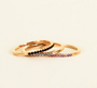 The Half Pave Ring - Black features a dainty gold band adorned with a row of shimmering black cubic zirconia, beautifully stacked against a plain light background.