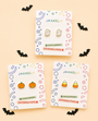Three sets of JaxKelly Ghost Enamel Flat Back Kids Earrings—featuring ghost shapes, pumpkins, and candy corn—are displayed on cards and surrounded by small black bat cutouts, all arranged on a light beige background. These playful kids’ earrings are crafted from surgical-grade stainless steel for comfort and safety.