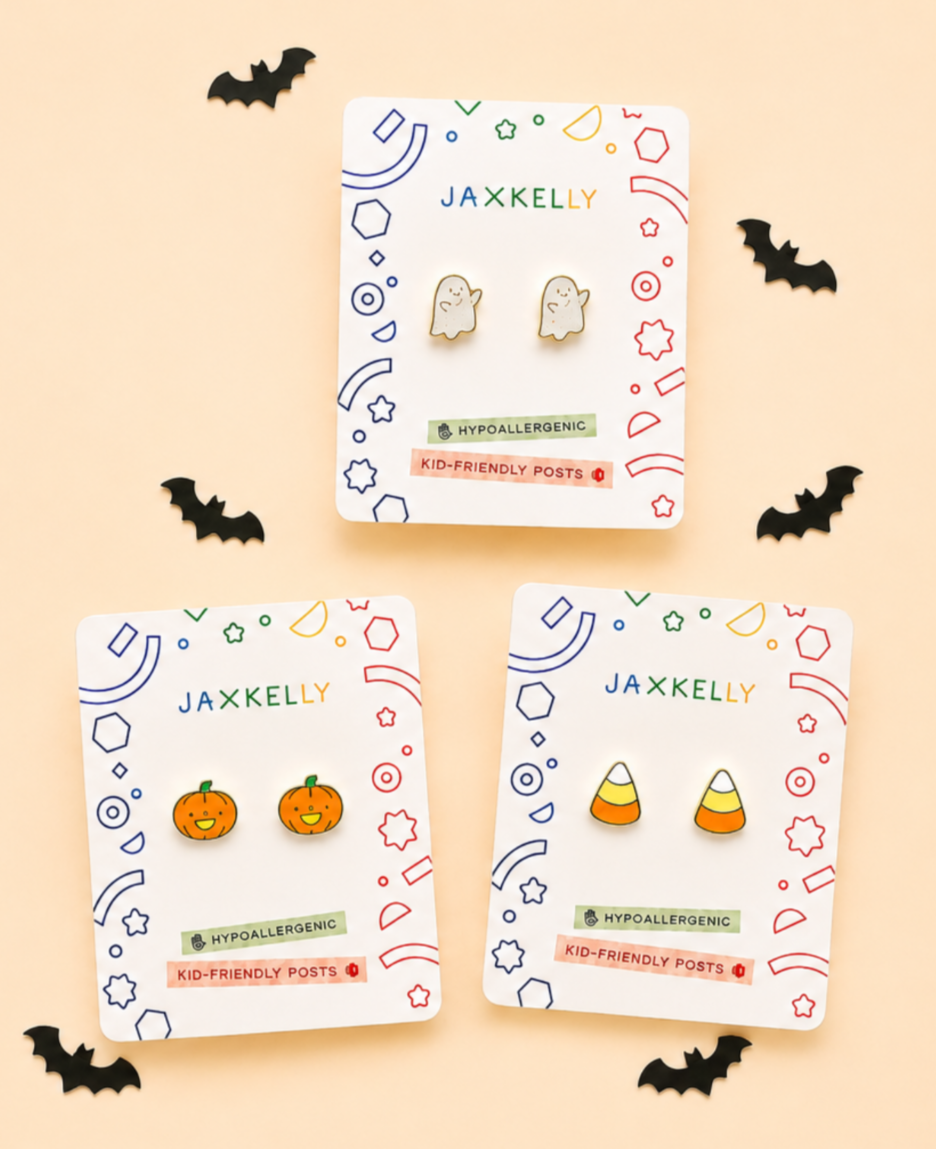 JaxKelly Pumpkin Enamel Flat Back Kids Earrings, displayed on brand cards and surrounded by small black paper bats against a peach background. These hypoallergenic earrings are perfect for kids with sensitive ears, ensuring comfortable and worry-free wear.