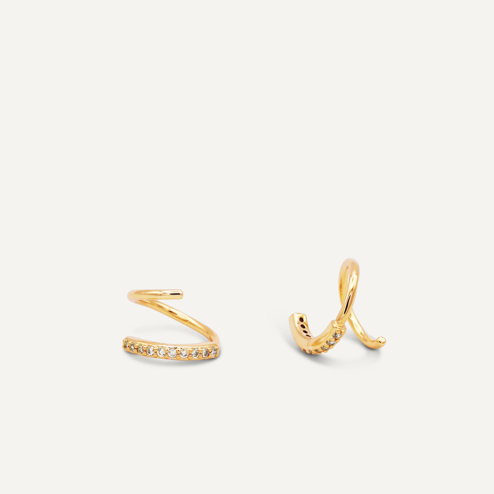 The Pave Spiral - Earring is shown on a white background, featuring two gold ear cuffs: one with a zigzag shape and pave stones, the other with a smooth spiral design adorned with sparkling stones along its edge.