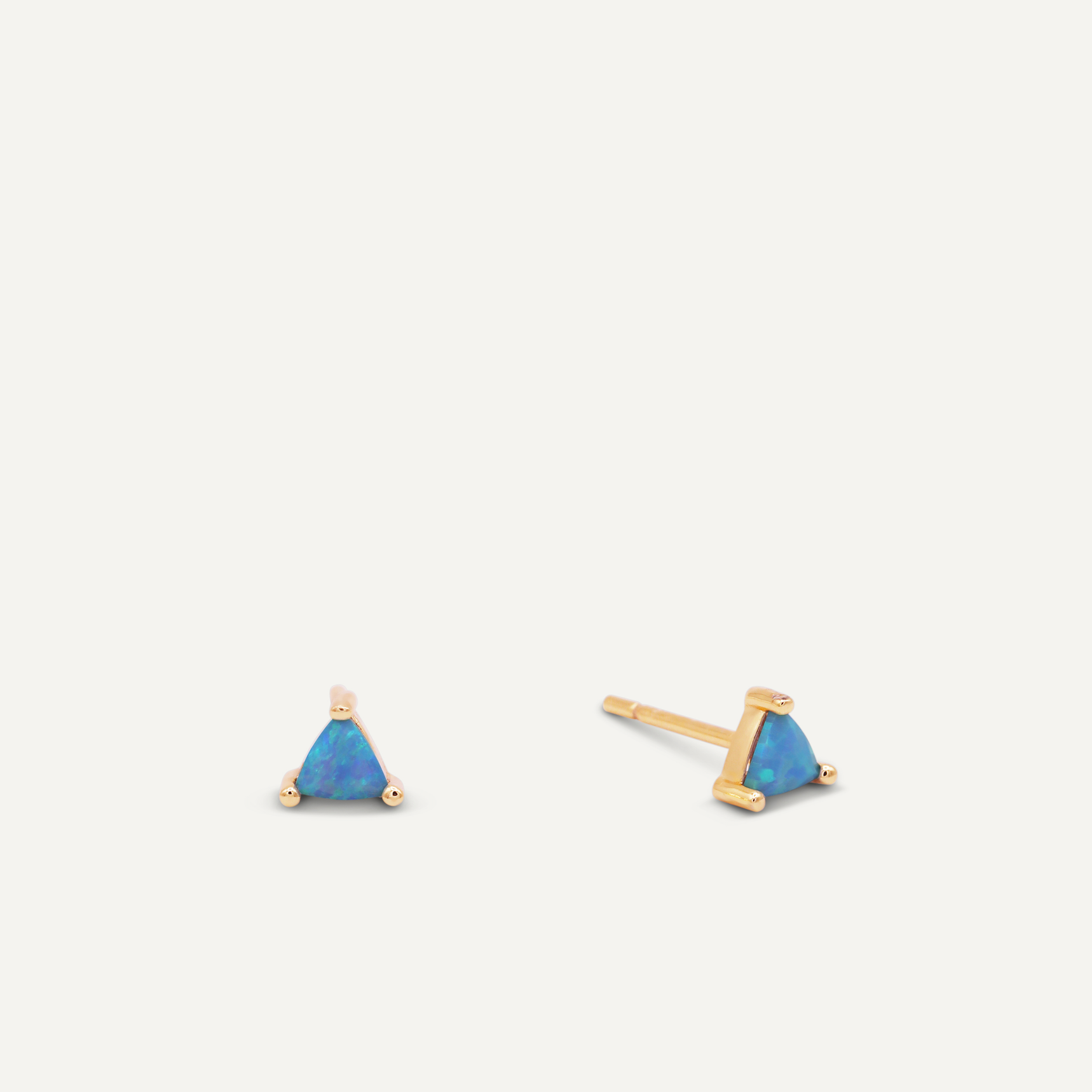 The Fire Opal Mini Energy Gems - Joy studs feature small, triangular lab-grown fire opals set in 18k gold plating. Displayed on a white background, one earring is shown from the front and the other from the side.