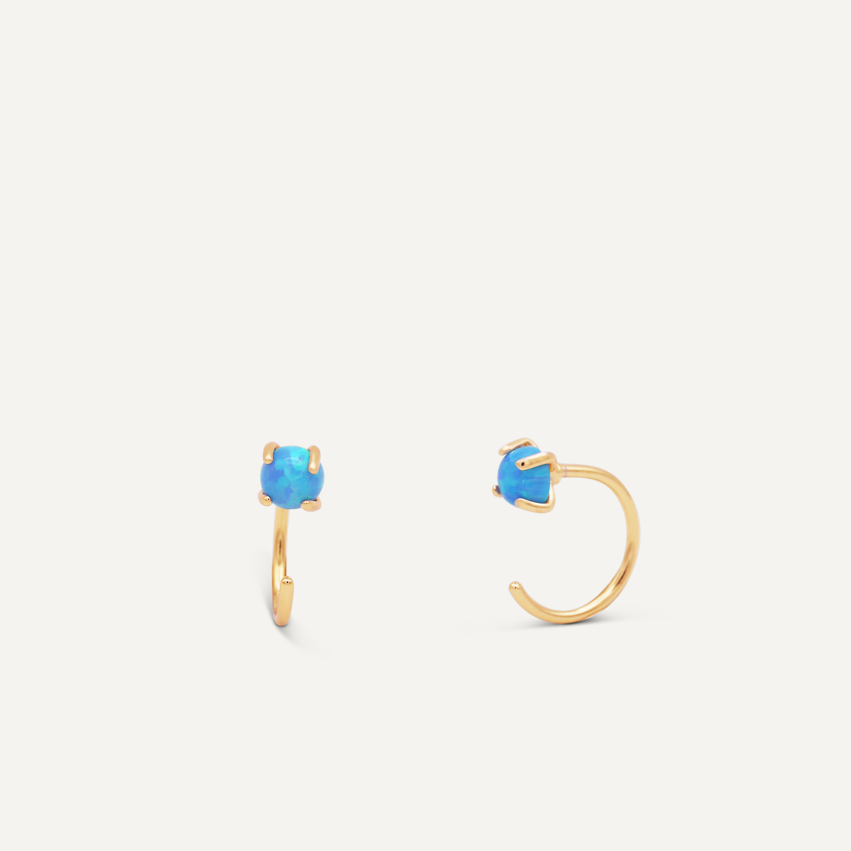 The Fire Opal Huggie features two gold plated earrings, each set with a single round lab-grown Fire Opal in a four-prong setting, shown on a plain white background.