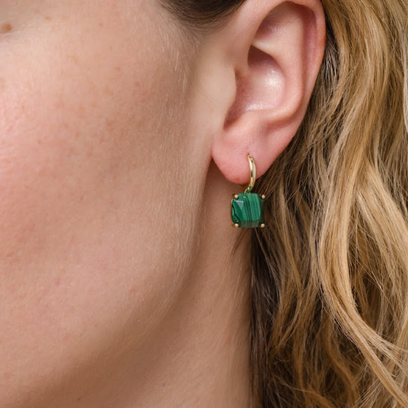 Close-up of a woman's ear wearing JaxKelly's Gemstone Mini Drop - Malachite earrings, featuring a rectangular green malachite gemstone in 18K gold plating. She has light skin and wavy blonde hair.