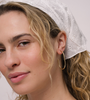 A woman with wavy blonde hair wears a white eyelet headscarf and the JaxKelly Gold Large Open Hoop earrings, looking into the camera with a slight smile against a neutral background.