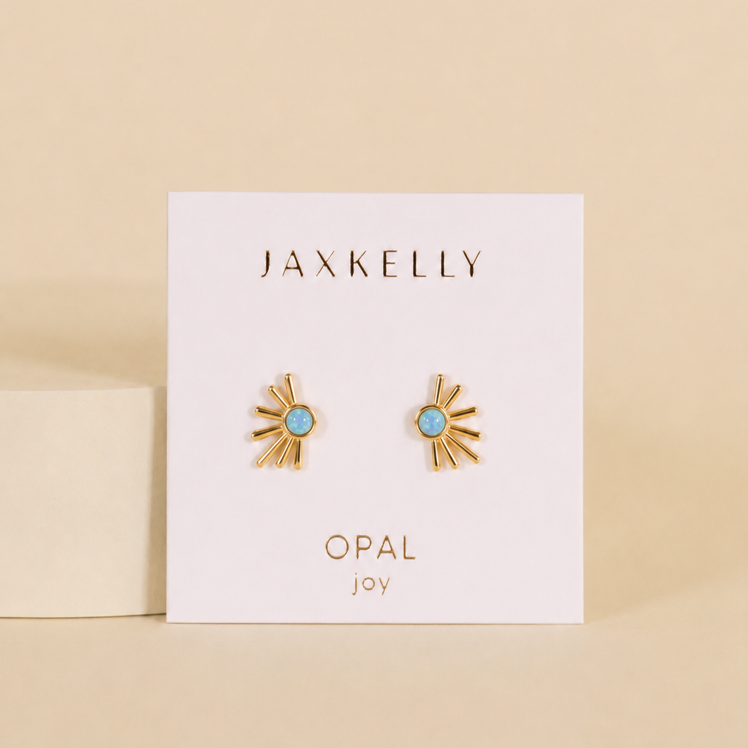 A pair of gold Sun Ray - Fire Opal earrings by JaxKelly, featured on a branded card against a beige background—stunning boho studs with radiant blue opal centers for any occasion.