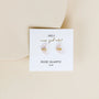 A pair of crescent-shaped rose quartz Mystery Earrings with gold wire detail is displayed on a white JaxKelly card labeled "wear good vibes: ROSE QUARTZ love, final sale," set against a light beige background.
