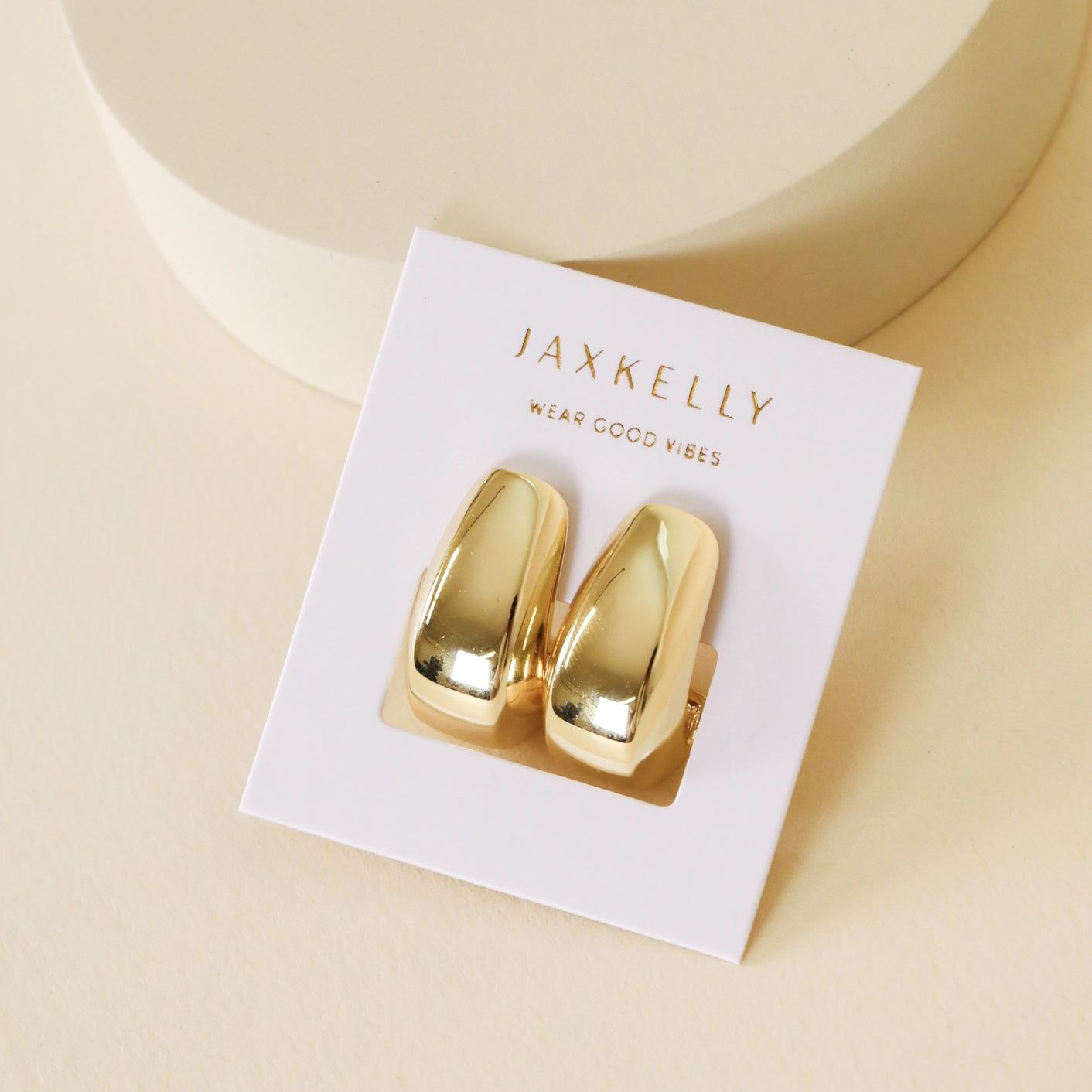The Bold Drop Earring features shiny gold-plated hoops with sterling silver posts, displayed on a JaxKelly card reading "WEAR GOOD VIBES," set against a neutral beige background.