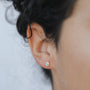 A close-up of a person’s ear with dark curly hair, wearing the Turquoise Sun Stud—a small gold earring featuring a turquoise stone center and sunburst design. The softly blurred background highlights the earring.