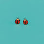 Ladybug Enamel Flat Back Kids Earrings in red and black, designed for sensitive ears, displayed on a bright turquoise background.