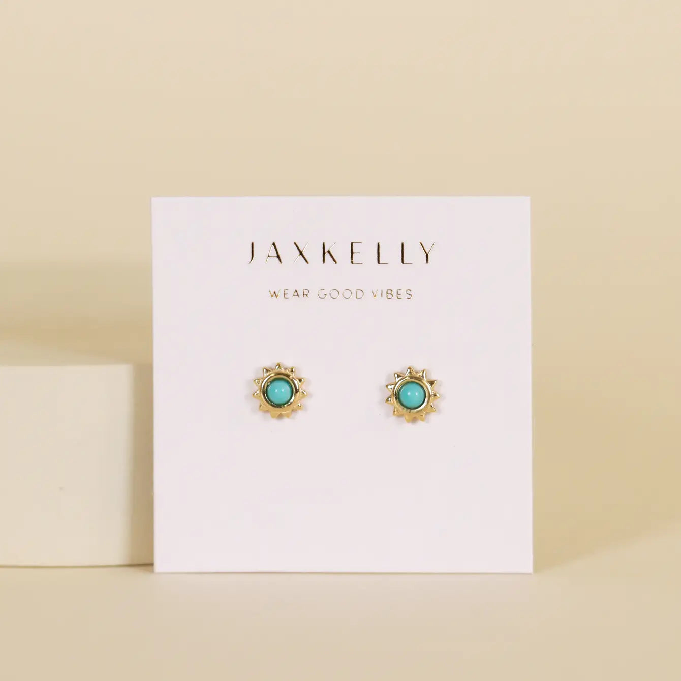 The Turquoise Sun Stud earrings feature gold sun designs with turquoise stone centers and 18k gold plating, displayed on a white JaxKelly "Wear Good Vibes" card against a beige background.