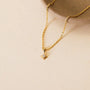 The JaxKelly Tiny Star Necklace, featuring an adjustable 18k gold plated chain with a small star-shaped Cubic Zirconia pendant, is shown on a neutral background beside a beige ceramic dish.