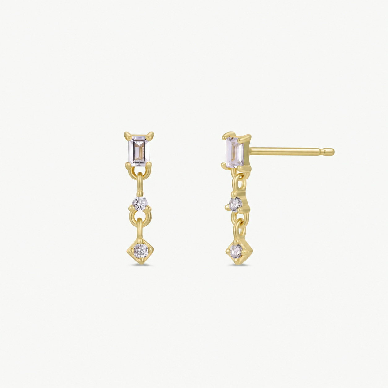 JaxKelly’s Mini Baguette Drop - White CZ earrings feature a vertical gold chain with small rectangular and round white CZ stones, displayed on a plain white background. Enjoy jewelry that stays brilliantly shiny and tarnish-free over time.