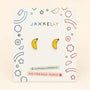 A pair of JaxKelly Banana Enamel Flat Back Kids Earrings for sensitive ears, displayed on a decorative card labeled “Hypoallergenic and Kid-Friendly Posts,” featuring colorful geometric designs around the edges.
