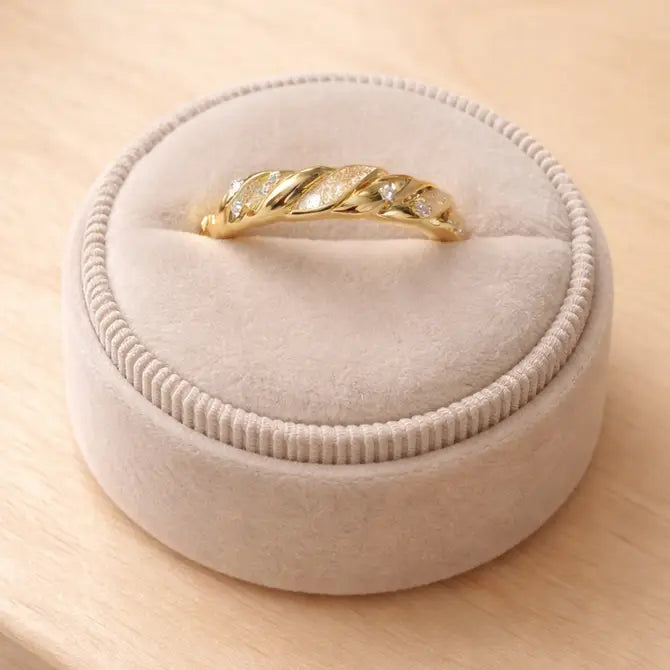 The Gold Twist Ring - White Opal features a twisted leaf design with diamond accents and a shimmering lab-grown opal, shown on a beige plush ring box set on light wood.