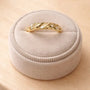 The Gold Twist Ring - White Opal features a twisted leaf design with diamond accents and a shimmering lab-grown opal, shown on a beige plush ring box set on light wood.