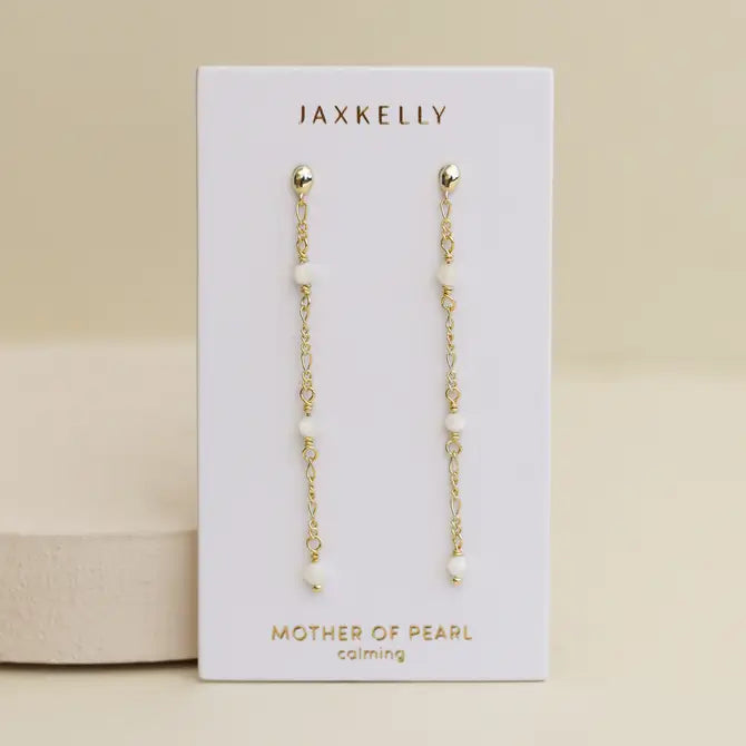 JaxKelly's Gemstone Chain Drop - Mother of Pearl earrings feature small white beads and 18k gold plating, displayed on a white card with "Mother of Pearl calming" in gold, set against a neutral background.