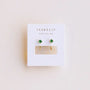 A pair of JaxKelly Emerald CZ Huggie earrings, 18k gold plated with small green stones, displayed on a white card featuring the WEAR GOOD VIBES slogan above the earrings.