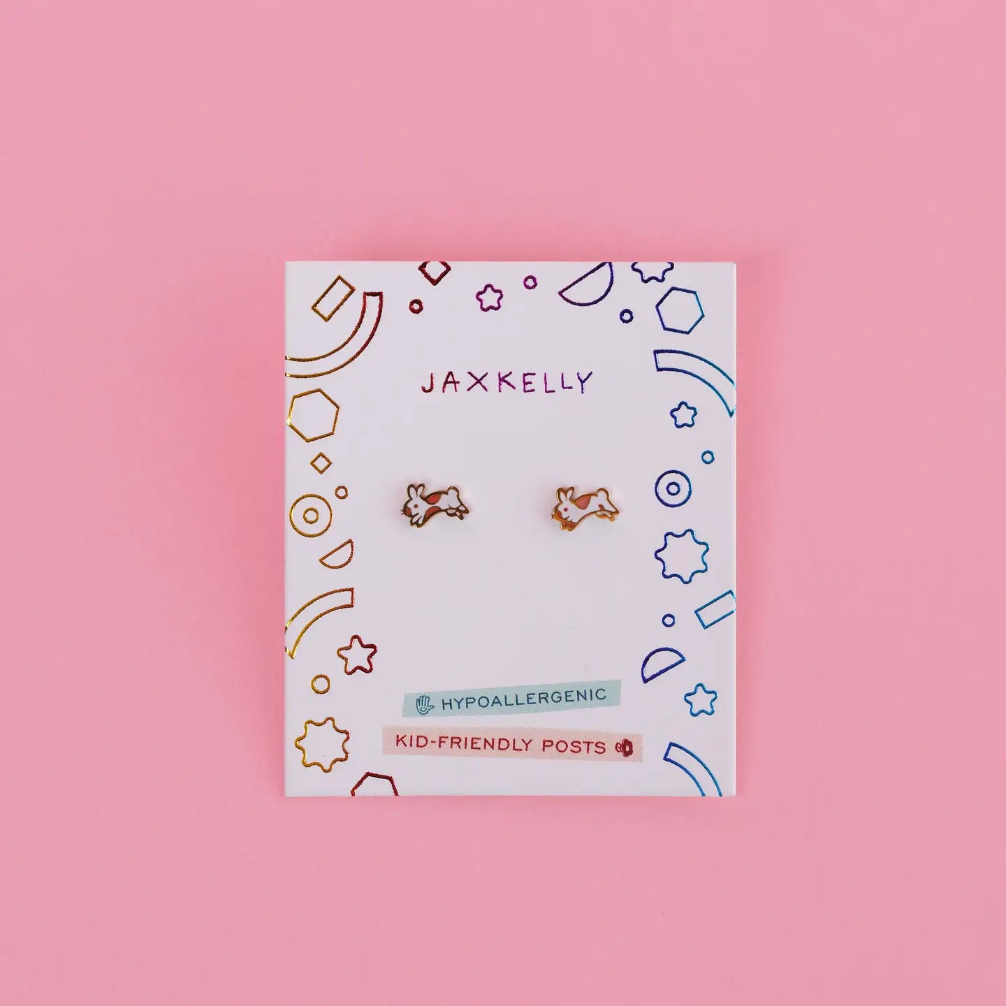 A pair of Bunny Enamel Flat Back Kids Earrings, small gold hypoallergenic studs shaped like bunnies, displayed on a white JaxKelly card with colorful designs and "Hypoallergenic" and "Kid-Friendly Posts" labels, set against a pink background.