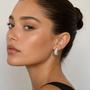 A woman with smooth, glowing skin and dark hair in a sleek bun wears a sleeveless black top and JaxKelly's Silver Bold Swirl Earrings, looking confidently at the camera against a neutral background.