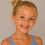 A young blonde girl smiles at the camera, wearing a light blue tank top and JaxKelly's Boot Enamel Charm Hoop earrings—fun, colorful hoops perfect for sensitive ears. The background is plain and neutral.