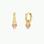 The Bow Enamel Charm Hoop features two small, hypoallergenic gold hoops, each with a pink and light gold enamel bow-shaped charm. These kids earrings are shown against a plain white background.