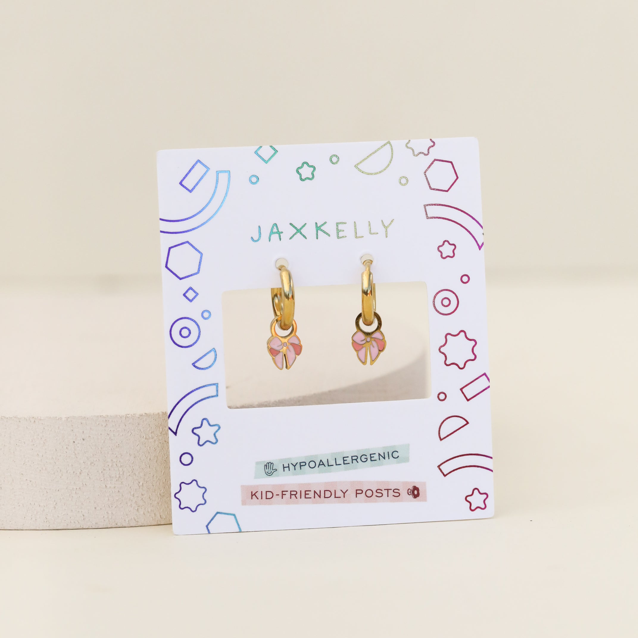 A pair of Bow Enamel Charm Hoop kids earrings with pink and yellow flower charms, displayed on a decorative JaxKelly card labeled Hypoallergenic and Kid-Friendly Posts.