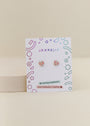 A pair of small, pink and gold Bow Enamel Flat Back Kids Earrings are shown on a white card with colorful geometric designs and the JaxKelly brand name. Labels indicate hypoallergenic, kid-friendly posts.