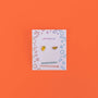 A pair of Lemon Enamel Flat Back Kids Earrings—one lemon slice and one orange slice—on a white JaxKelly card with colorful doodles, set against an orange background. Fun, playful and hypoallergenic!.