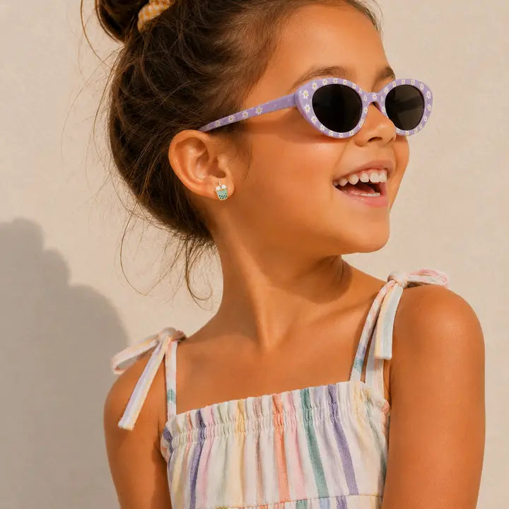 Smiling young girl wearing purple sunglasses, a colorful striped summer dress, and JaxKelly Matcha Boba Tea Enamel Flat Back Kids Earrings, looking to the side with her hair in a bun against a light background.