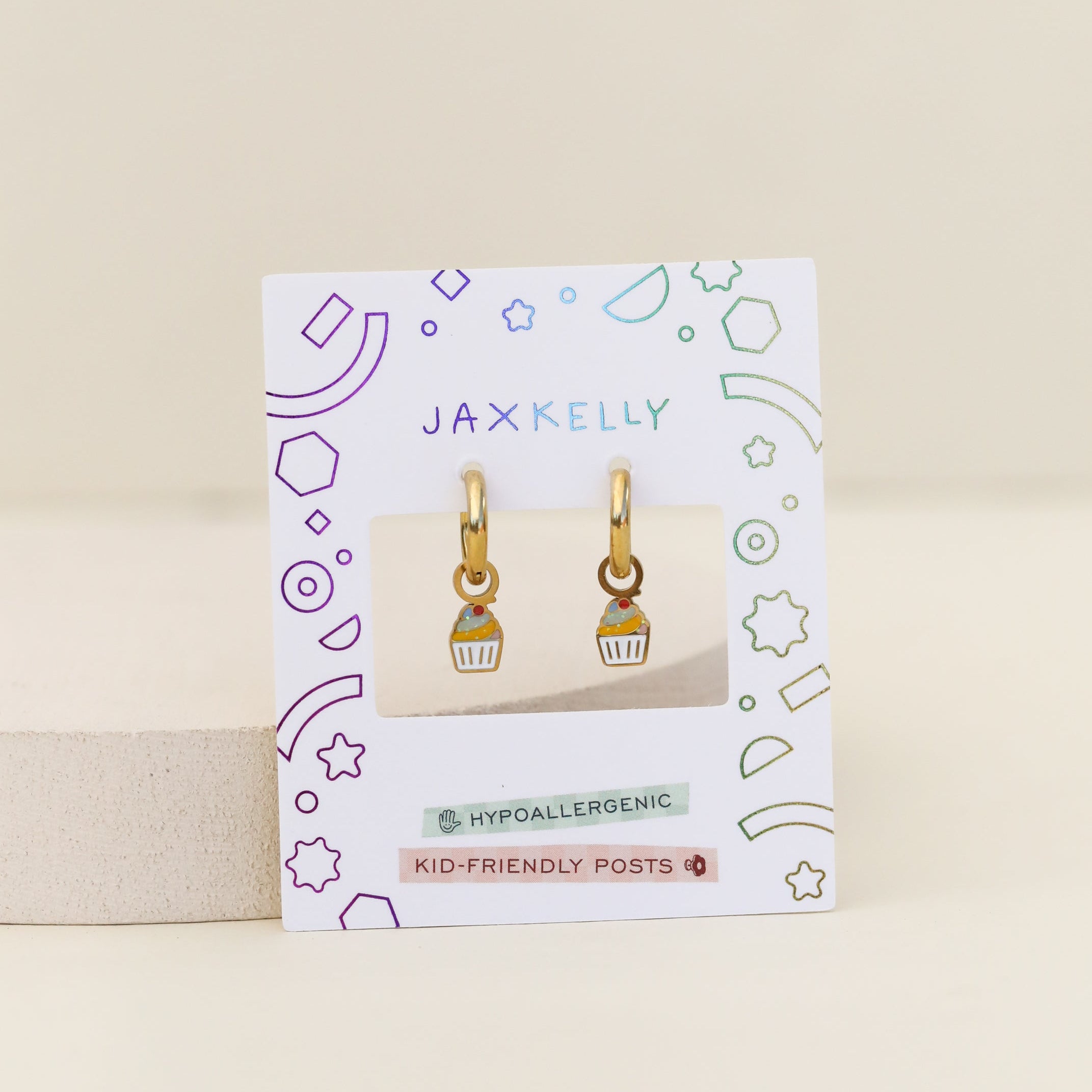 Cupcake Enamel Charm Hoop earrings on a white JaxKelly card with colorful geometric designs. The card notes hypoallergenic, kid-friendly posts—ideal for little ones with sensitive ears.