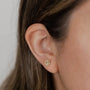 Close-up of a woman's ear with brown hair, wearing JaxKelly's Pavé Peace Sign earring—a small, circular gold stud adorned with sparkling CZ stones and finished in 18k gold plating. The softly blurred background highlights its elegance.