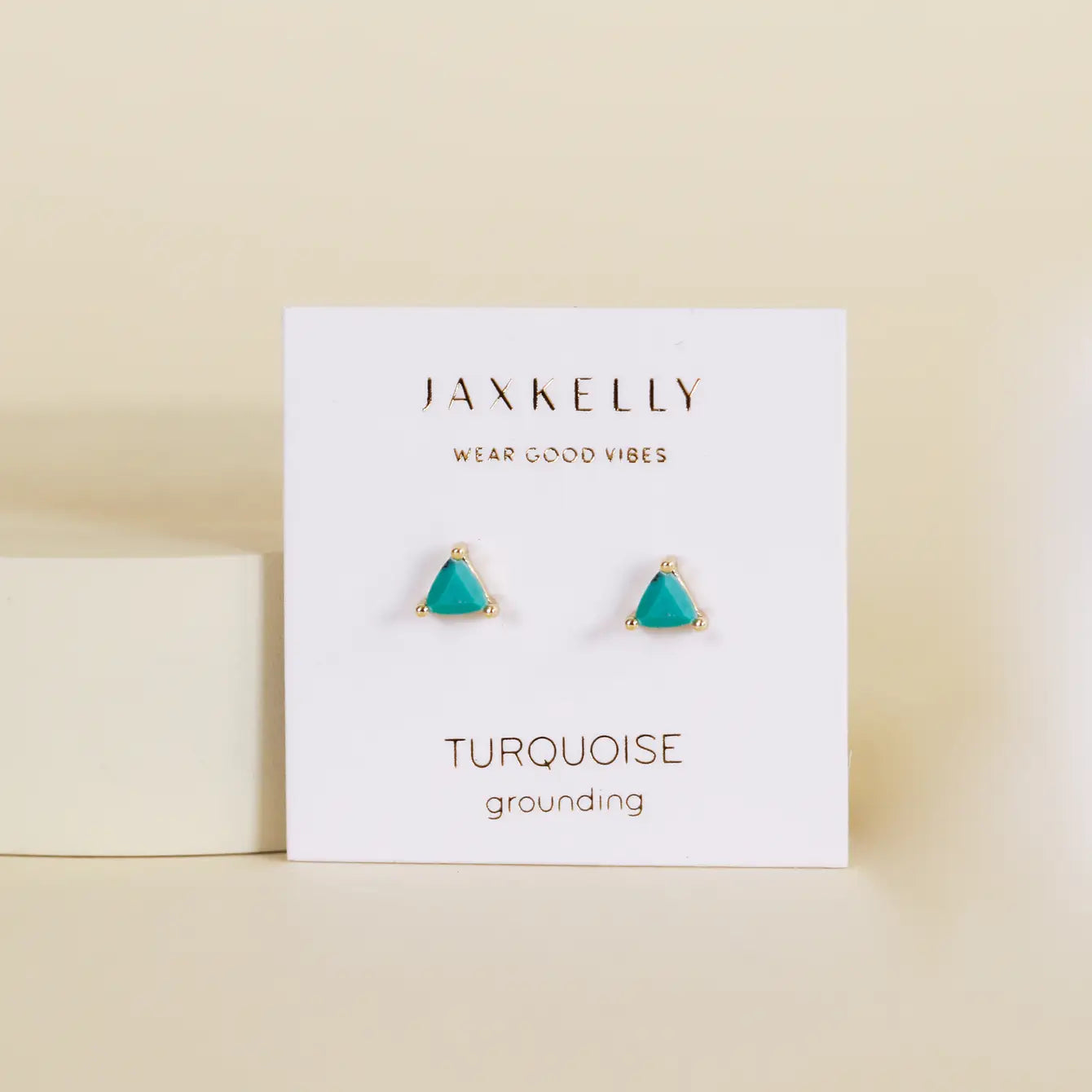 A pair of Turquoise - Mini Energy Gem studs with small triangular turquoise stones, 18k gold plating, and sterling silver posts on a white JaxKelly card reading "Wear Good Vibes" and "Turquoise grounding" against a soft beige background.