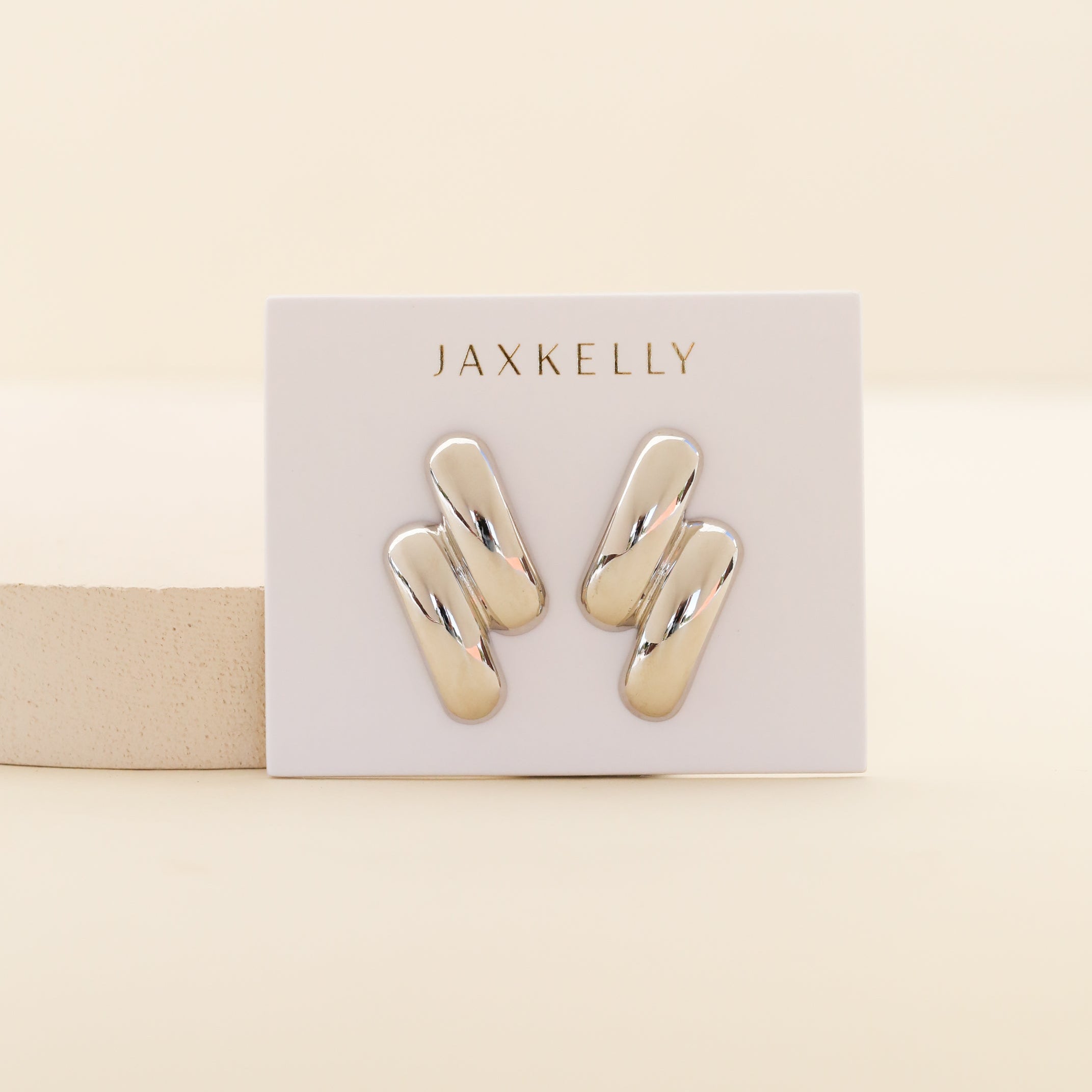 A pair of shiny, rhodium plated Silver Double Bold Bar earrings displayed on a white card with JAX KELLY in gold lettering, set against a neutral beige background—perfect tarnish-free jewelry for any collection.