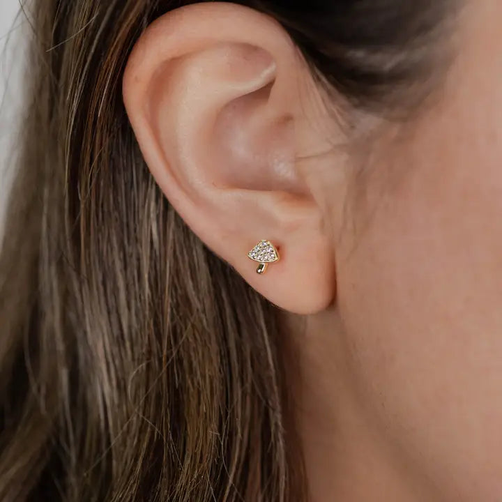 Close-up of a person with light skin and brown hair wearing JaxKelly’s Pavé Mushroom stud earring—a small, gold-plated jewelry piece shaped like a mushroom with sparkling pavé detail.