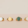 Four JaxKelly Mother of Pearl Signet Rings, each 18k gold plated with a unique color—white, gold, green, or pale pinkish-white—are displayed on a soft beige background.