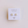 A pair of small gold-plated White Opal Crown Stud earrings by JaxKelly, displayed on a white card with "Wear Good Vibes" and "Opal Joy" printed on it.