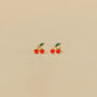 Cherry Enamel Flat Back Kids Earrings: Gold stud earrings shaped like cherries with two red enamel fruits and a green enamel leaf. Hypoallergenic and perfect for kids or sensitive ears, shown on a plain beige background.