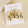A pair of Gold Bold Wave sculptural stud earrings by JaxKelly, with 18k gold plating and a modern abstract wave design, displayed on a white card printed with JaxKelly and "Wear Good Vibes" in gold letters.