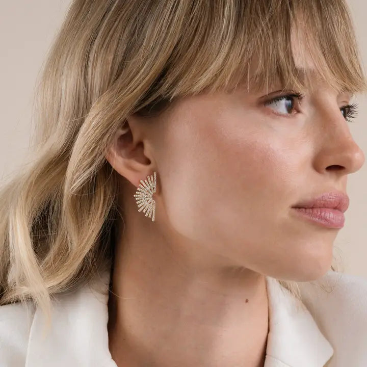 A woman with blonde hair wears a cream top and JaxKelly Sunburst Studs—large gold vermeil earrings with pearl accents—while looking to the right against a neutral background.