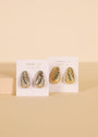Two pairs of textured hoop earrings, including the Silver Bold Swirl Earring and a gold fluted drop design, are shown on white JaxKelly cards against a beige background.