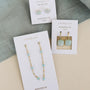 Three pairs of JaxKelly earrings are shown on cards: Round Amazonite Gemstone Gold Earrings, gold-plated dangle earrings with blue stones, and gold huggie earrings with square blue stones.