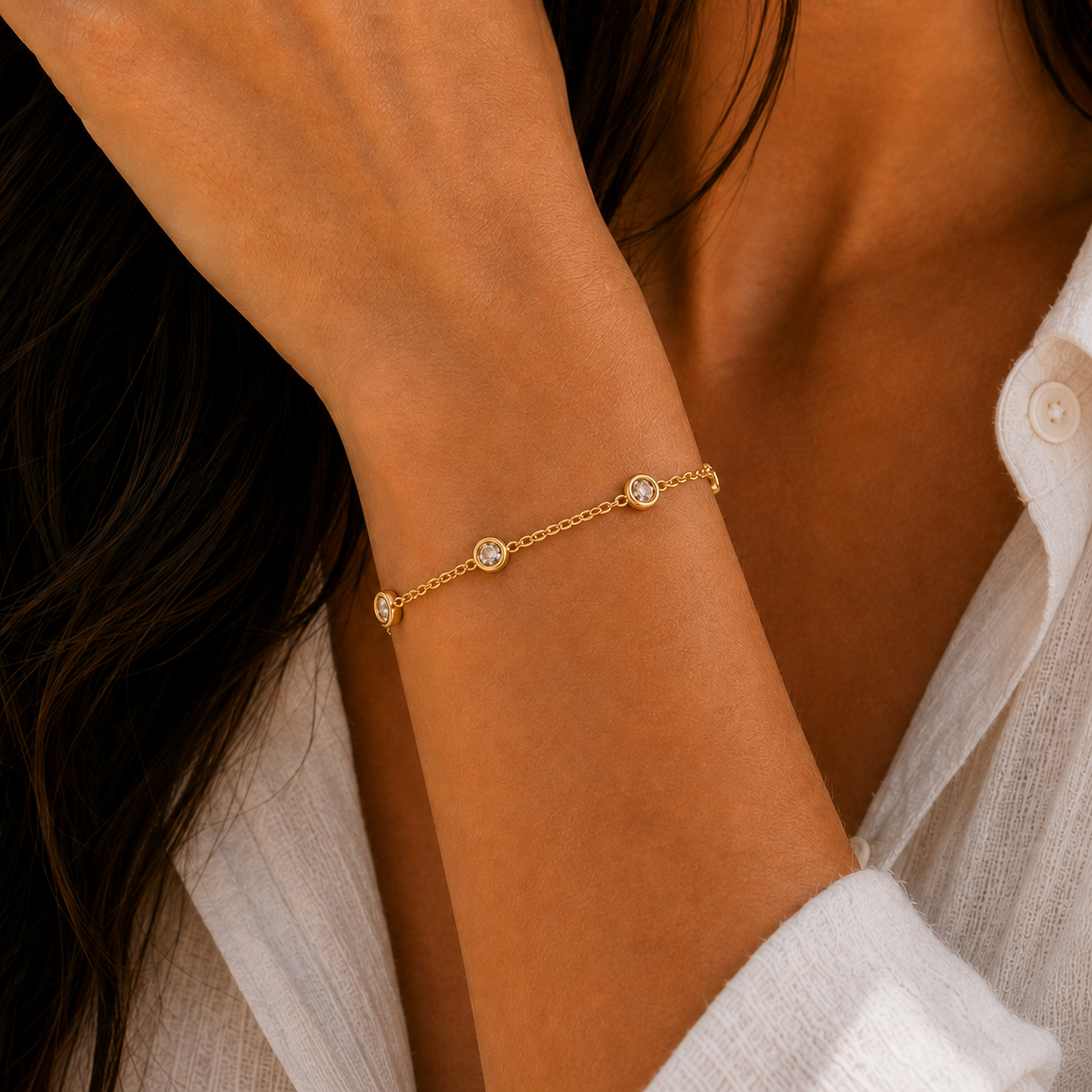 A person wearing a white textured shirt showcases the JaxKelly Champagne Gemstone Bracelet— a delicate gold-plated piece adorned with evenly spaced champagne stones.