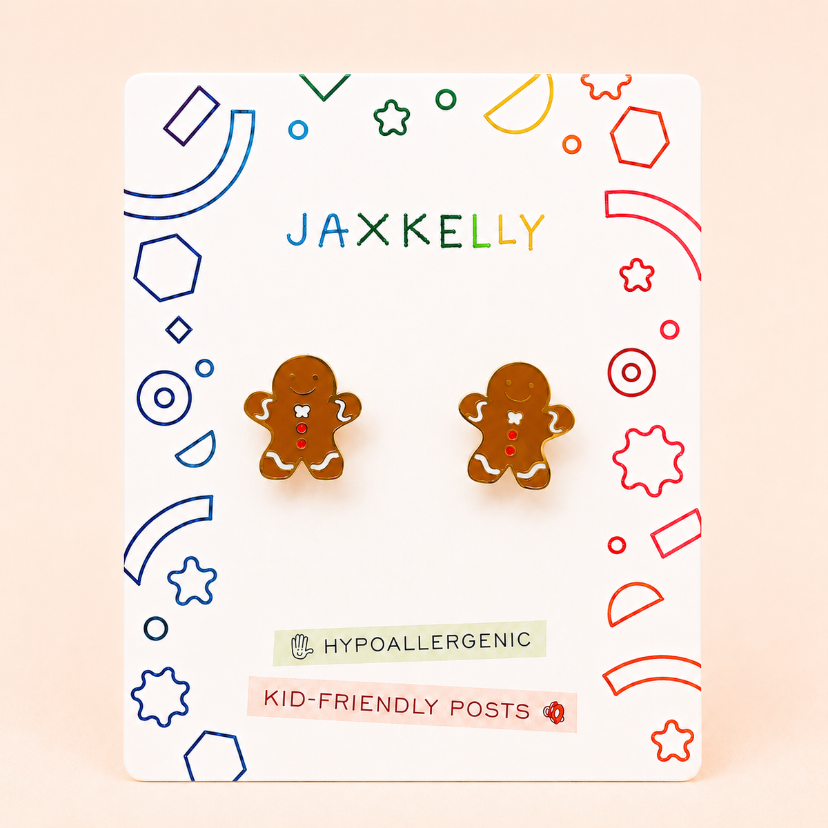 A pair of JaxKelly Gingerbread Man Enamel Flat Back Kids Earrings are displayed on a card with colorful geometric designs, labeled surgical-grade stainless steel hypoallergenic earrings with kid-friendly posts.