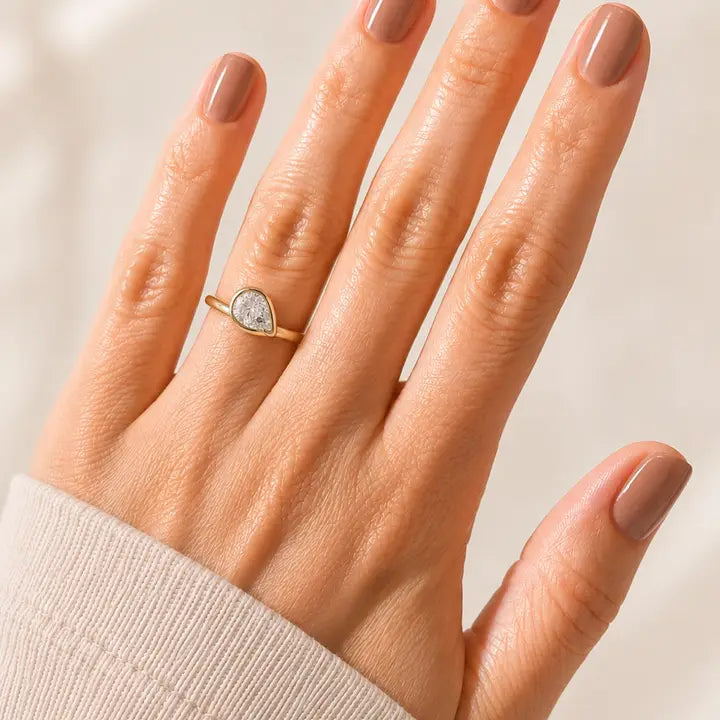 JaxKelly Halo Drop Gold Ring - White CZ with a pear-cut crystal on a finger.