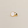 The White Opal Signet Ring by JaxKelly features a large oval white opal set in 18k gold plating, showcased on a simple beige background.