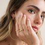 A young woman with natural makeup and light brown hair touches her face, wearing JaxKelly's Illusion Double Hoop - Gold Earrings, a gold ring, a delicate necklace, and showing off her freckles.