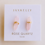A pair of minimalist rose quartz earrings with gold wire wrapping, displayed on a white card reading "JaxKelly Rose Quartz Mineral Point - Love"—elegant everyday jewelry from JaxKelly.