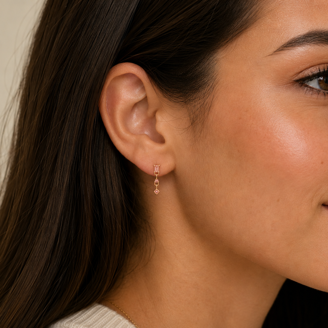 Close-up of a woman’s ear adorned with JaxKelly’s Mini Baguette Drop - Champagne CZ earrings. Her long dark hair is tucked back, highlighting the sparkling, tarnish-free gold and geometric elegance of this beautiful accessory.